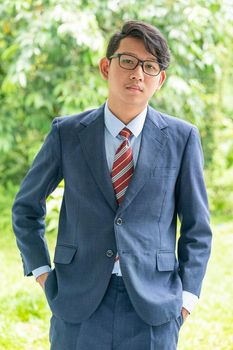 Young asian business men portrait in suit and wear eyeglasses standing outside in a park during sunny day