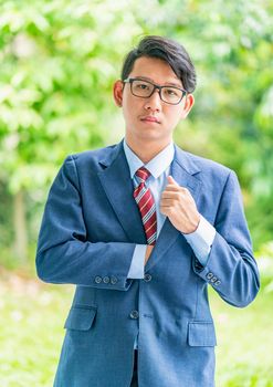 Young asian business men portrait in suit and wear eyeglasses standing outside in a park during sunny day