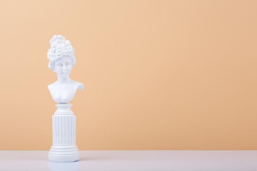White gypsum statue on white table against beige background with copy space. High quality photo