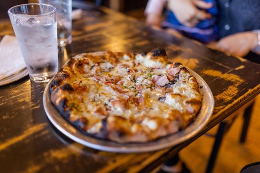 Tasty small cheese pizza with slightly burnt edge on vintage-looking wooden table. Delicious Italian dish and two glasses of cold water on rustic wooden surface. Food and drinks