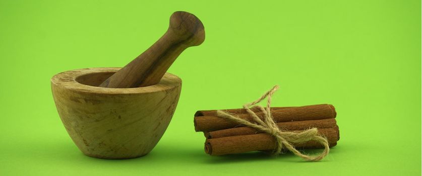 Cinnamon sticks bundle tied with jute string and wooden mortar with pestle on green background and free copy space for text