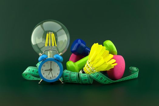 Starting healthy lifestyle idea concept with lamp light bulb, alarm clock and various sports inventory including dumbbells weights, shuttlecock and measuring tape over a dark green background