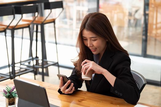 Cropped shot of female business holding cup and using smartphone on wooden table in cafe