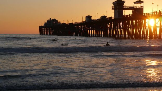 Oceanside, California USA - 16 Feb 2020: Surfer silhouette, pacific ocean beach in evening, water waves and sunset. Tropical coastline, waterfront vacation resort. People enjoy surfing as sport hobby.
