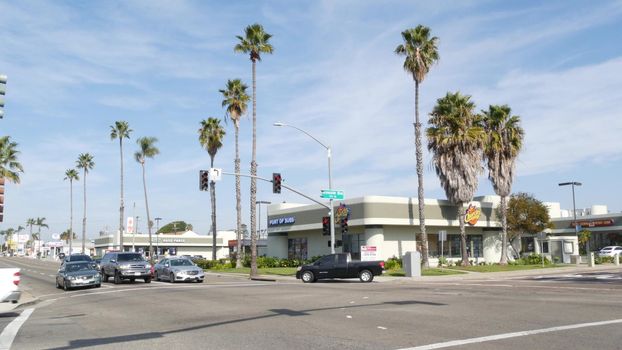 Oceanside, California USA - 27 Jan 2020: Palm trees on Route 101 american highway, pacific coast tropical street. Traffic light and auto transport on road intersection, cars on crossroad in suburb.
