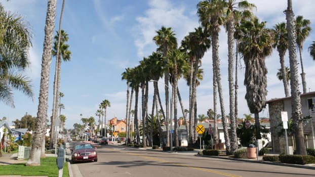 Oceanside, California USA - 27 Jan 2020: Palm trees on typical american street, pacific coast tropical resort. Auto transport on road, generic city view. Railroad level crossing, railway red signal.