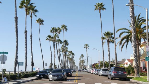 Oceanside, California USA - 16 Feb 2020: Cars on road and people walking, waterfront promenade. Pacific ocean tropical beach tourist resort with palm trees. Beachfront street on sunny summer day.