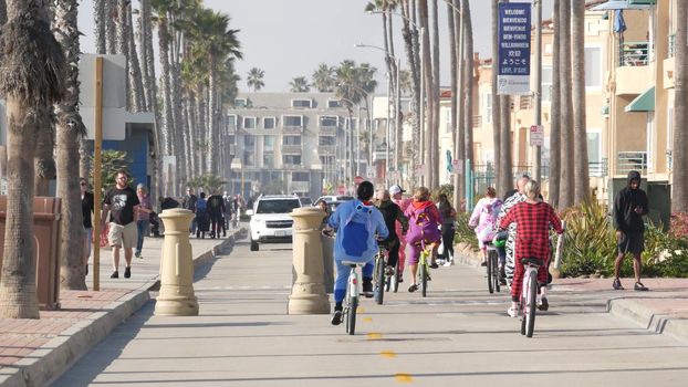 Oceanside, California USA - 8 Feb 2020: People walking on waterfront promenade, beachfront boardwalk near pier. Vacations ocean beach resort near Los Angeles. People in pajama riding bikes or bicycles