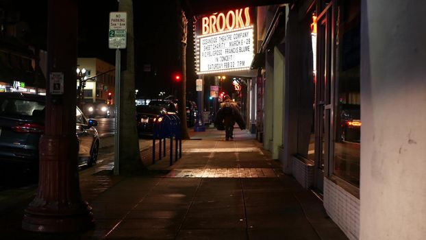 Oceanside, California USA - 9 Feb 2020: Lonely man looks like homeless walking, city street walkway at night. Male person on sidewalk, possible unemployed jobless beggar. Poverty and begging problem.