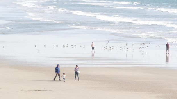 Oceanside, California USA - 11 Feb 2020: Local people walking strolling, pacific ocean coast, beach from pier. Sea water waves tide, shore sand. Beachfront vacations resort. Waterfront promenade.