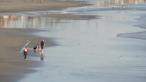 Oceanside, California USA - 11 Feb 2020: Local people walking strolling, pacific ocean coast, beach from pier. Sea water waves tide, shore sand. Beachfront vacations resort. Waterfront promenade.
