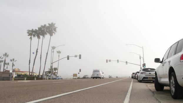 Encinitas, California USA -20 Feb 2020: Traffic light semaphore on highway 101 road by misty beach. Fog on sea shore, pacific ocean coast. Freeway with cars along shoreline, coastline near Los Angeles