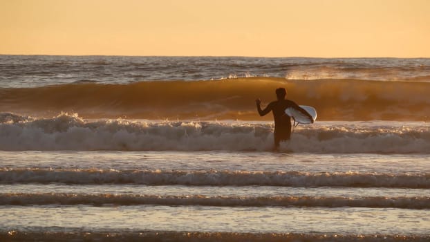 Oceanside, California USA - 27 Dec 2019: Surfer silhouette, pacific ocean beach in evening, water waves and sunset. Tropical coastline, waterfront vacation resort. People enjoy surfing as sport hobby.