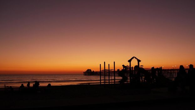 Oceanside, California USA - 8 Feb 2020: Silhouette of people making bbq campfire. Beachfront recreation area for barbeque with fire place on pacific ocean coast. Bonfire for barbecue on sunset beach.