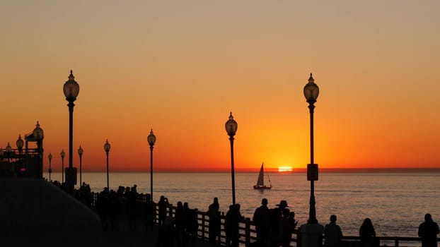Oceanside, California USA - 17 Nov. 2019: Wooden pier and people walking. Tourists strolling in waterfront resort, summertime vacations near Los Angeles. Sunset ocean beach, tropical sunny orange sky.