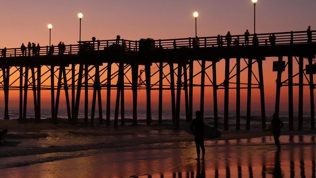 Oceanside, California USA - 16 Feb 2020: Surfer silhouette, pacific ocean beach in evening, water waves and sunset. Tropical coastline, waterfront vacation resort. People enjoy surfing as sport hobby.