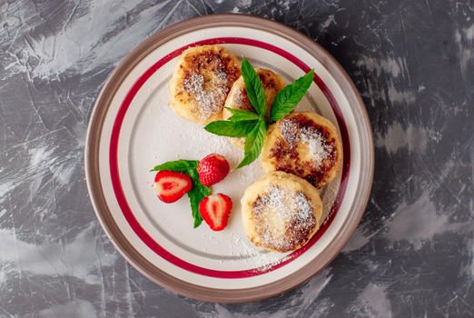 Gourmet breakfast - curd pancakes, cheesecakes, curd pancakes with strawberries, mint and icing sugar in a white plate. Selective focus. Top view.