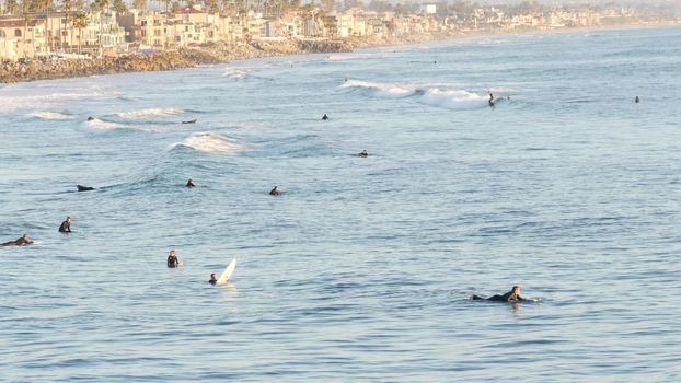Oceanside, California USA - 16 Feb 2020: People surfing, surfers swimming in water and waiting sea wave, standing on surfboard. Aquatic sport hobby, healthy lifestyle. Pacific ocean tropical resort.