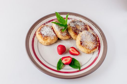 Gourmet breakfast - cottage cheese pancakes, cheesecakes, cottage cheese pancakes with strawberries, mint and powdered sugar in a white plate. Useful dessert on white background isolate