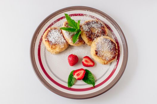 Gourmet breakfast - cottage cheese pancakes, cheesecakes, cottage cheese pancakes with strawberries, mint and powdered sugar in a white plate. Useful dessert on white background isolate