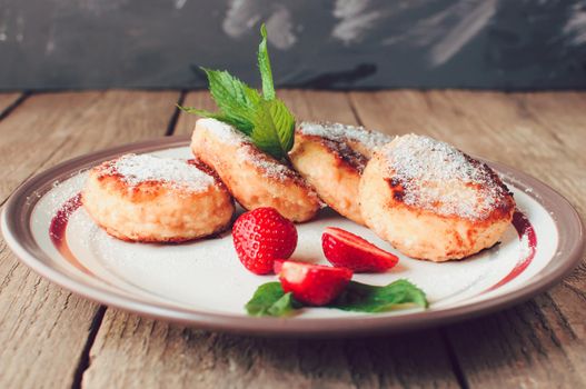 Gourmet breakfast - cottage cheese pancakes, cheesecakes, cottage cheese pancakes with strawberries, mint and powdered sugar in a white plate. Selective focus.