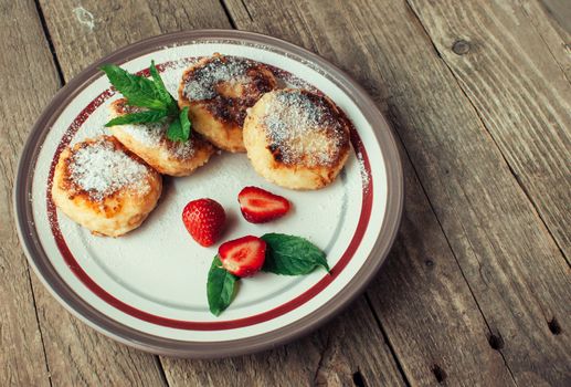 Gourmet breakfast - cottage cheese pancakes, cheesecakes, cottage cheese pancakes with strawberries, mint and powdered sugar in a white plate. Selective focus.