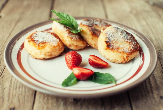 Gourmet breakfast - cottage cheese pancakes, cheesecakes, cottage cheese pancakes with strawberries, mint and powdered sugar in a white plate. Selective focus.