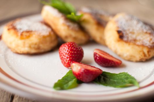 Gourmet breakfast - cottage cheese pancakes, cheesecakes, cottage cheese pancakes with strawberries, mint and powdered sugar in a white plate. Selective focus.