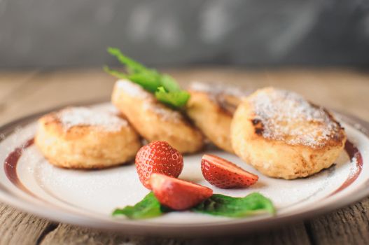 Gourmet breakfast - cottage cheese pancakes, cheesecakes, cottage cheese pancakes with strawberries, mint and powdered sugar in a white plate. Selective focus.