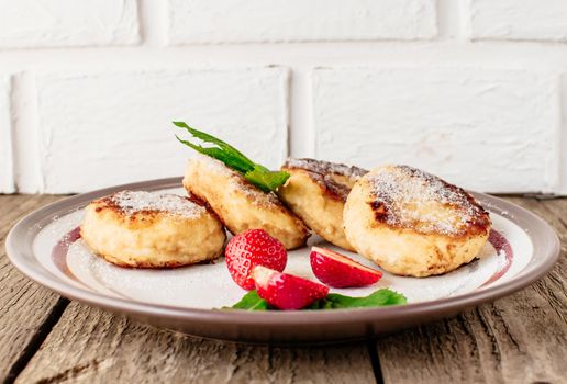 Gourmet breakfast - cottage cheese pancakes, cheesecakes, cottage cheese pancakes with strawberries, mint and powdered sugar in a white plate. Selective focus.