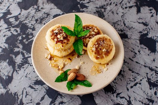 Cheesecakes, cottage cheese pancakes with almonds, fresh mint and maple syrup on a gray background from a concrete table. Cheesecakes, homemade traditional Ukrainian and Russian cheesecakes, top view.