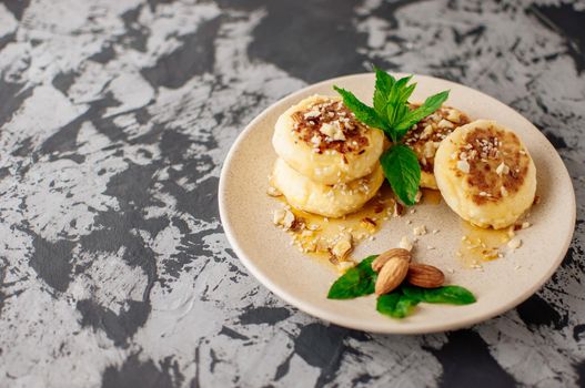 Cheesecakes, cottage cheese pancakes with almonds, fresh mint and maple syrup on a gray background from a concrete table. Cheesecakes, homemade traditional Ukrainian and Russian cheesecakes, top view.