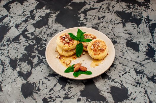 Cheesecakes, cottage cheese pancakes with almonds, fresh mint and maple syrup on a gray background from a concrete table. Cheesecakes, homemade traditional Ukrainian and Russian cheesecakes