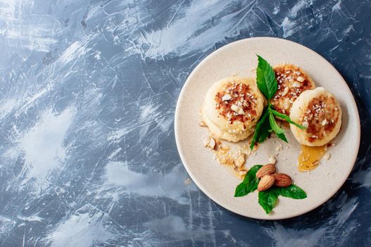 Cheesecakes,cottage cheese pancakes with almonds,fresh mint and maple syrup on a gray background from a concrete table copy space. Cheesecakes, homemade traditional Ukrainian and Russian cheesecakes