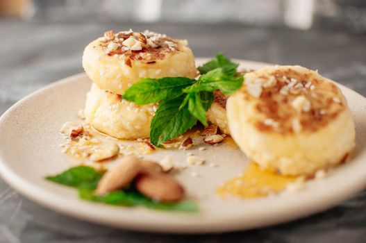 Cheesecakes,cottage cheese pancakes with almonds,fresh mint and maple syrup on a gray background from a concrete table. Cheesecakes, homemade traditional Ukrainian and Russian cheesecakes