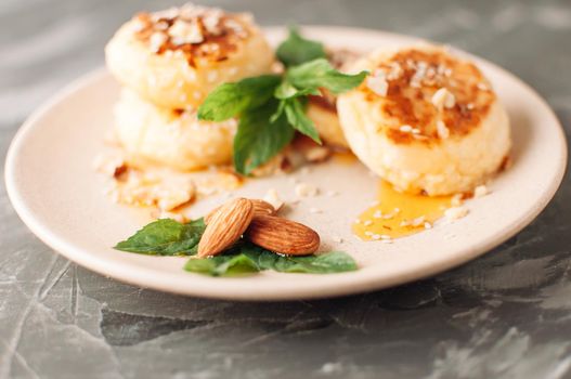 Cheesecakes,cottage cheese pancakes with almonds,fresh mint and maple syrup on a gray background from a concrete table. Cheesecakes, homemade traditional Ukrainian and Russian cheesecakes