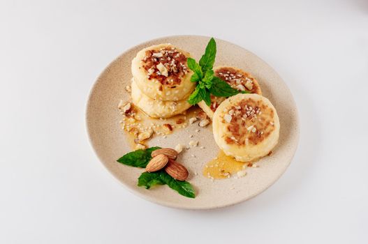 Delicious breakfast - cottage cheese pancakes, cheesecakes, cottage cheese pancakes with almonds, mint and maple syrup in a beige plate. Useful dessert on white background isolate
