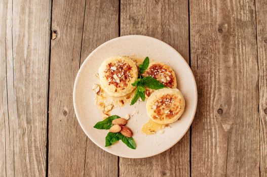 Delicious breakfast - cottage cheese pancakes,cheesecakes, cottage cheese pancakes with almonds, mint and maple syrup in a beige plate.Useful dessert on a wooden table in rustic style.Selective focus.