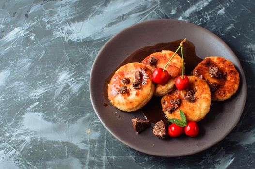 Breakfast Food Tasty Concept. Cheesecakes, cheesecakes, cottage cheese pancakes with cherries and chocolate on a black background concrete table. Close-up.Healthy food