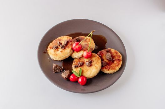 Gourmet breakfast - curd pancakes, cheesecakes, curd pancakes with cherries and chocolate in a brown plate. Healthy dessert on a white background isolate
