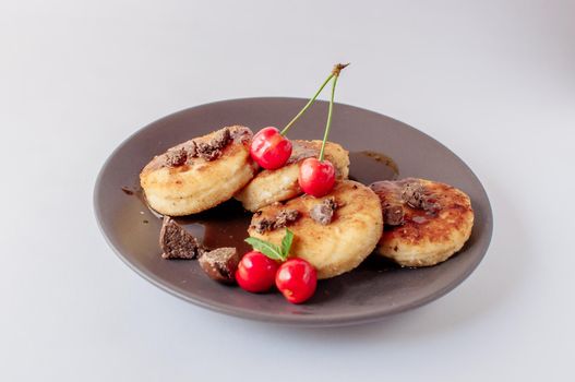 Gourmet breakfast - curd pancakes, cheesecakes, curd pancakes with cherries and chocolate in a brown plate. Healthy dessert on a white background isolate