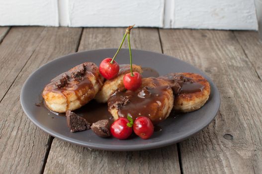 Gourmet breakfast - curd pancakes, cheesecakes, curd pancakes with cherries and chocolate in a brown plate. Wholesome dessert on a wooden table in a rustic style. Selective focus