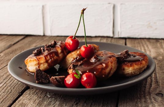 Breakfast Food Tasty Concept. Cheesecakes, cheesecakes, curd pancakes with cherries and chocolate on a black background from a concrete table and a white brick wall. Close-up.Healthy Food