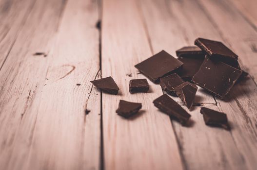 dark chocolate without sugar and gluten free for diabetics and allergics. Black chocolate broken into pieces lies on a white table in a rustic style. Dark toning and vignette.