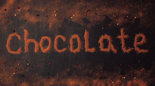 inscription chocolate made of cocoa powder with the addition of pieces of chocolate, chocolate powder, red, black and white pepper on a black graphite background