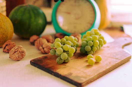 Autumn still life.Green grapes lie on wooden board.In the background are pumpkins,walnuts and scales.Autumn harvest concept.Happy Thanksgiving.Selective focus.Horizontal orientation.