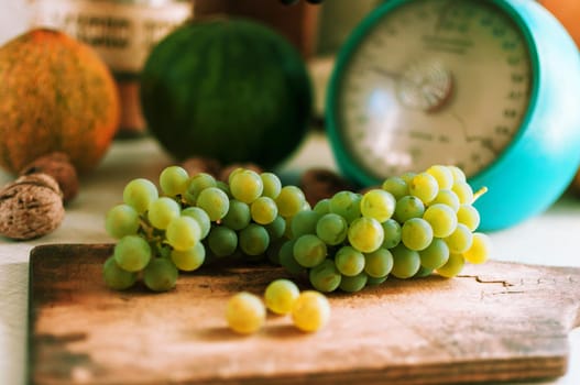 Autumn still life.Green grapes lie on wooden board.In the background are pumpkins,walnuts and scales.Autumn harvest concept.Happy Thanksgiving.Selective focus.Horizontal orientation.