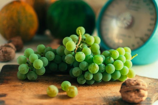 Autumn still life.Green grapes lie on wooden board.In the background are pumpkins,walnuts and scales.Autumn harvest concept.Happy Thanksgiving.Selective focus.Horizontal orientation.