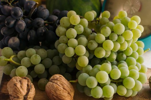 Autumn still life with grapes on a wooden board and walnuts around on a wooden white table. On the back scales. The concept of autumn harvest. Happy Thanksgiving. Selective focus. Template for design.