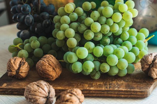 Autumn still life with grapes on a wooden board and walnuts around on a wooden white table. On the back scales. The concept of autumn harvest. Happy Thanksgiving. Selective focus. Template for design.